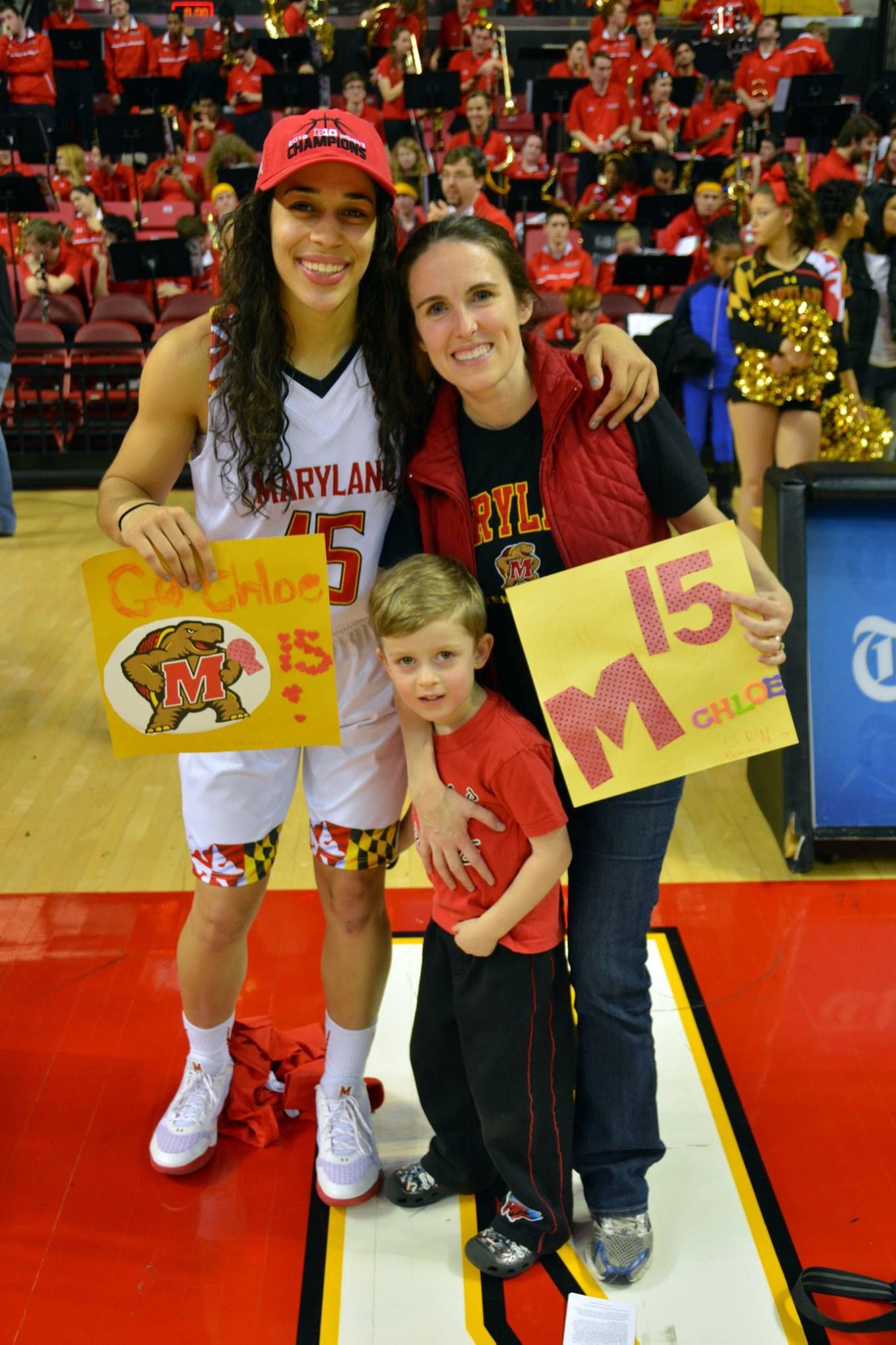 Sports fans in red team gear pose with signs at a basketball game.