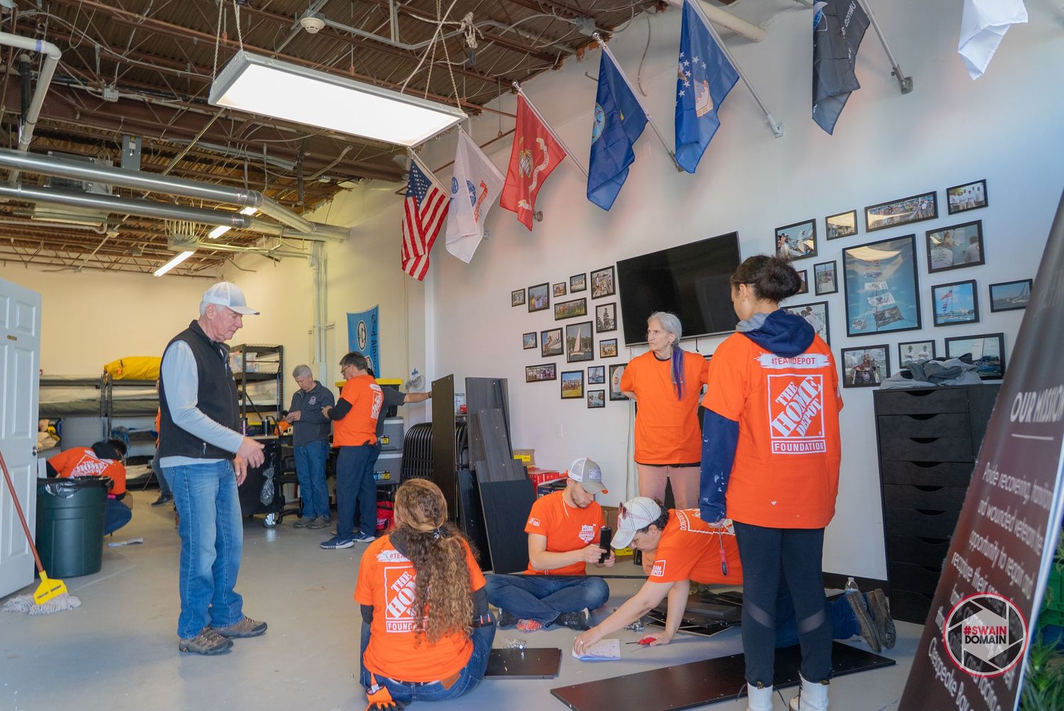 Volunteers in orange Home Depot aprons working together on community service projects in an indoor space.