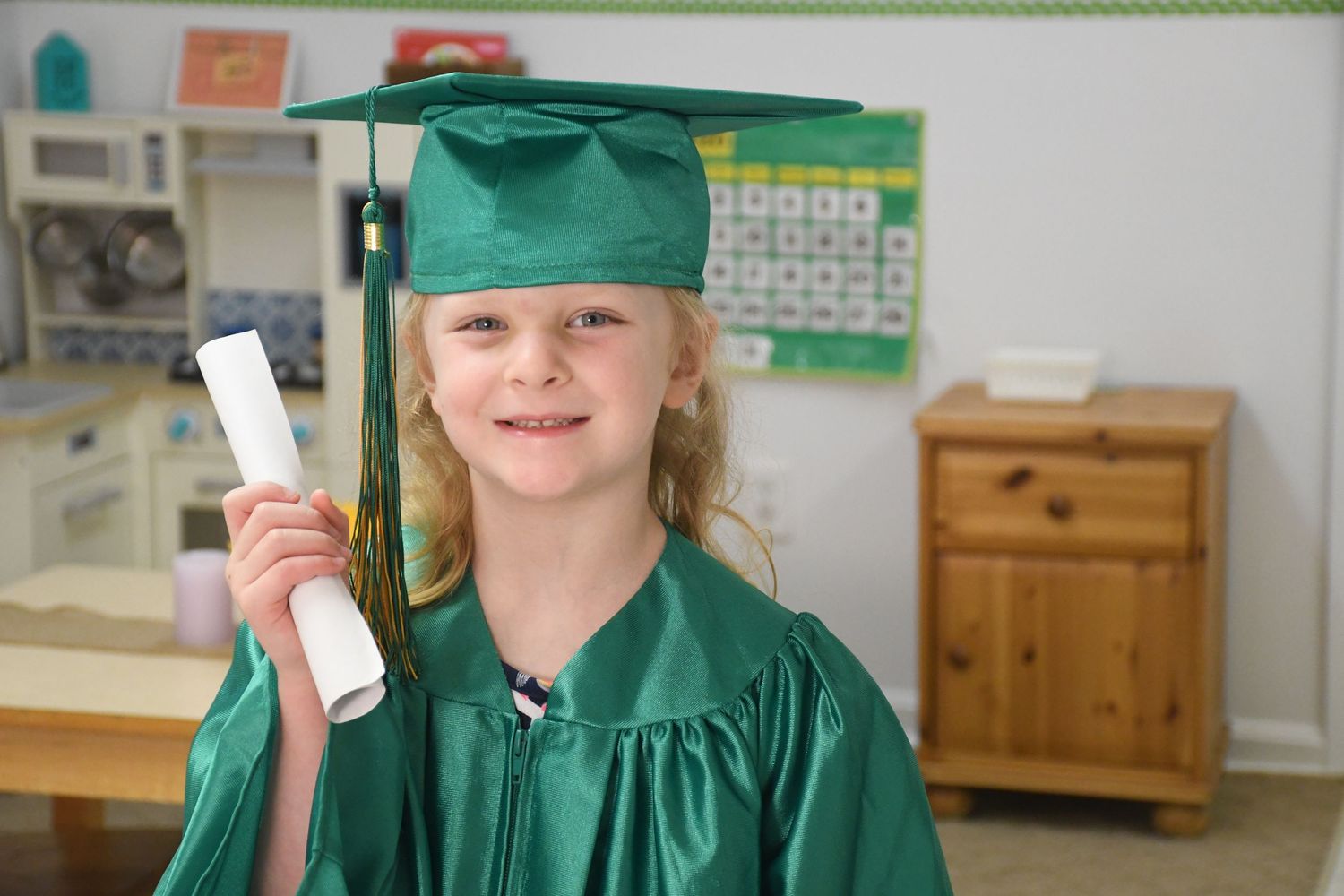 Young graduates in green caps and gowns posing with diplomas.