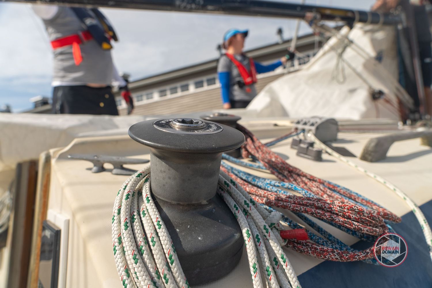 Close-up view of black sailing winch with colorful rope wrapped around it on a boat deck.