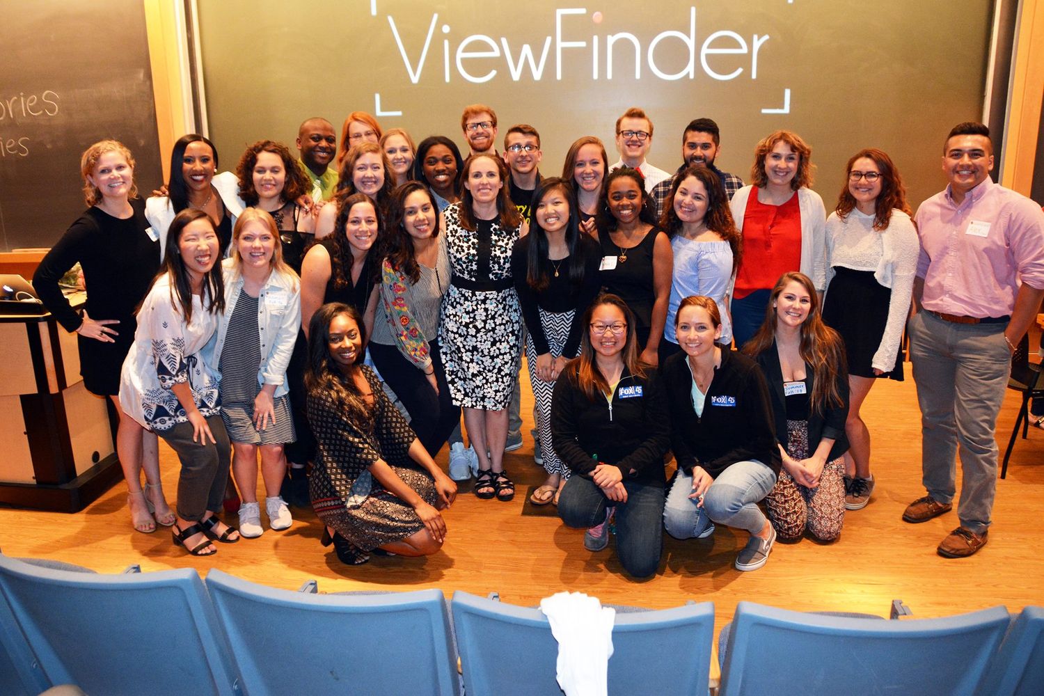 Large group of students pose together for a group photo in a classroom.