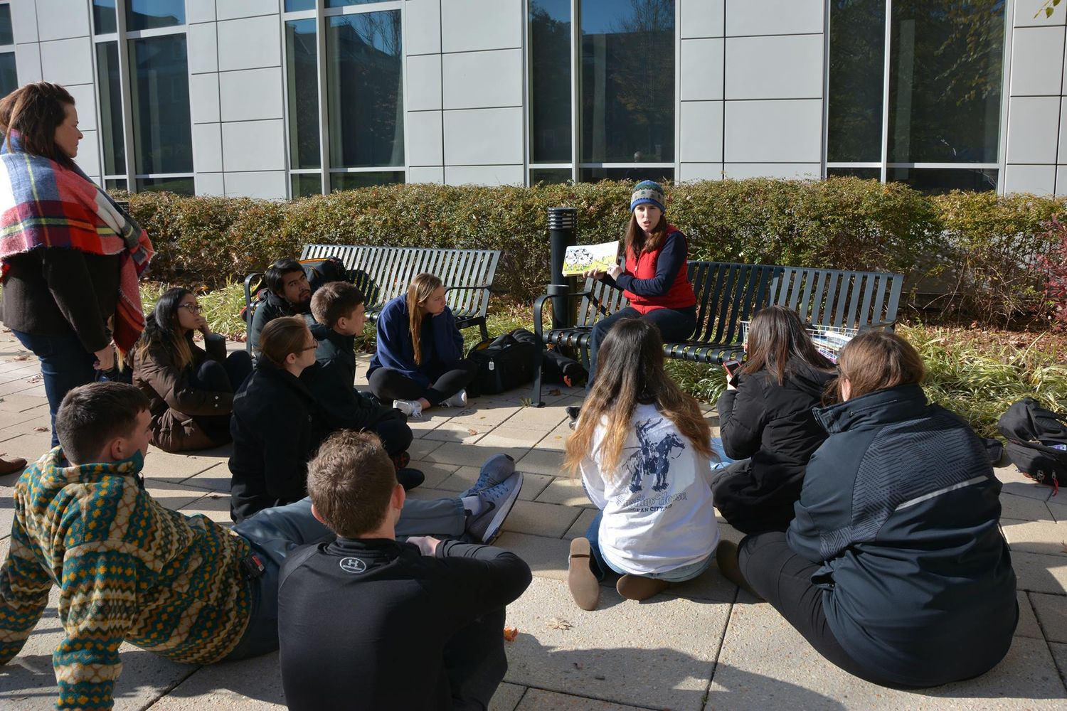 Students sit outdoors on steps in front of a modern building.