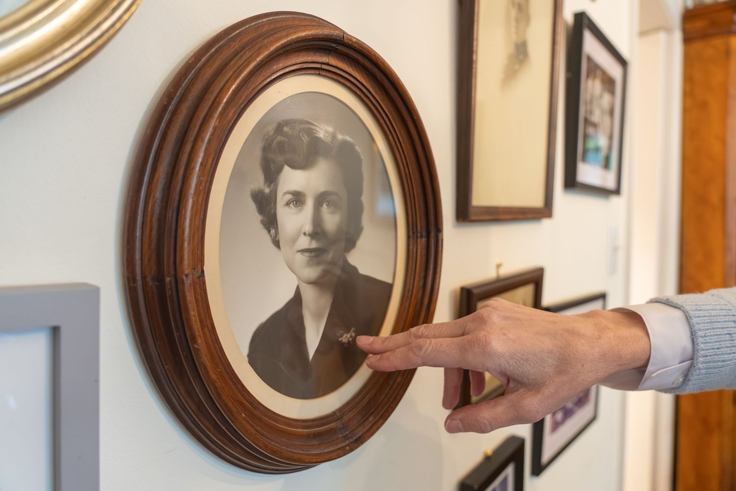 A hand points to a vintage oval-framed portrait of a woman hanging on a wall gallery.
