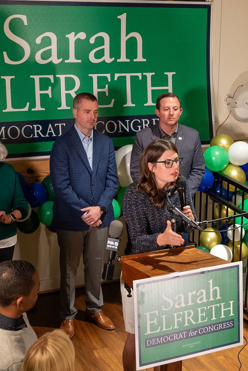 Campaign event setup with green Sarah Lefreth for Congress signs and supporters.