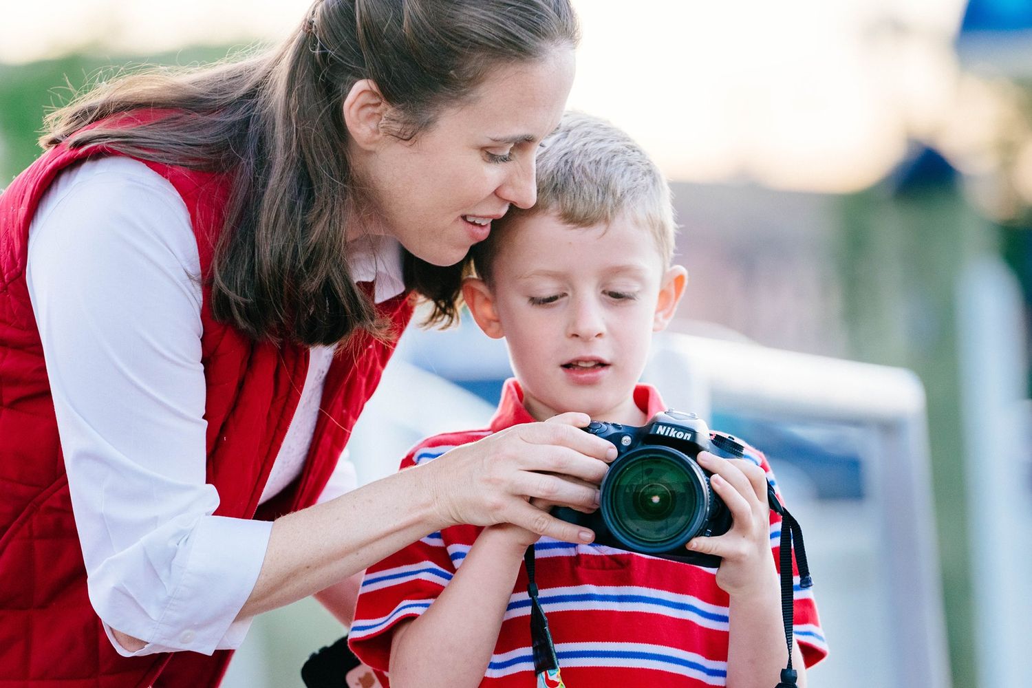 Parent and child looking through camera viewfinder together during outdoor photography lesson.
