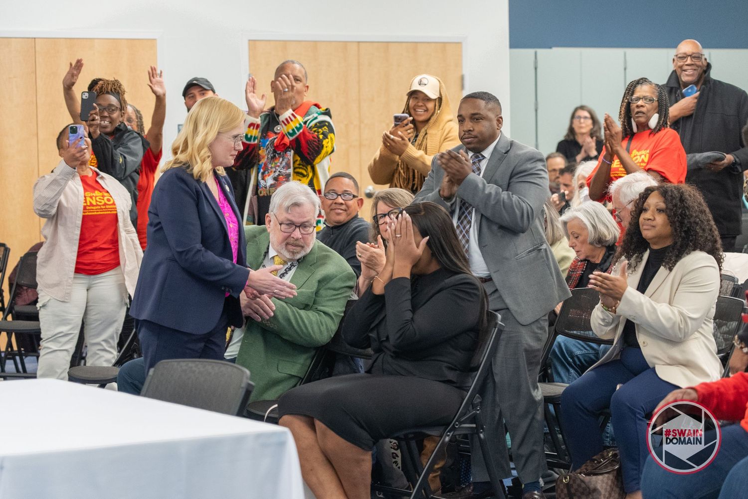 Engaged audience members participate in a community gathering with raised hands and enthusiastic expressions.