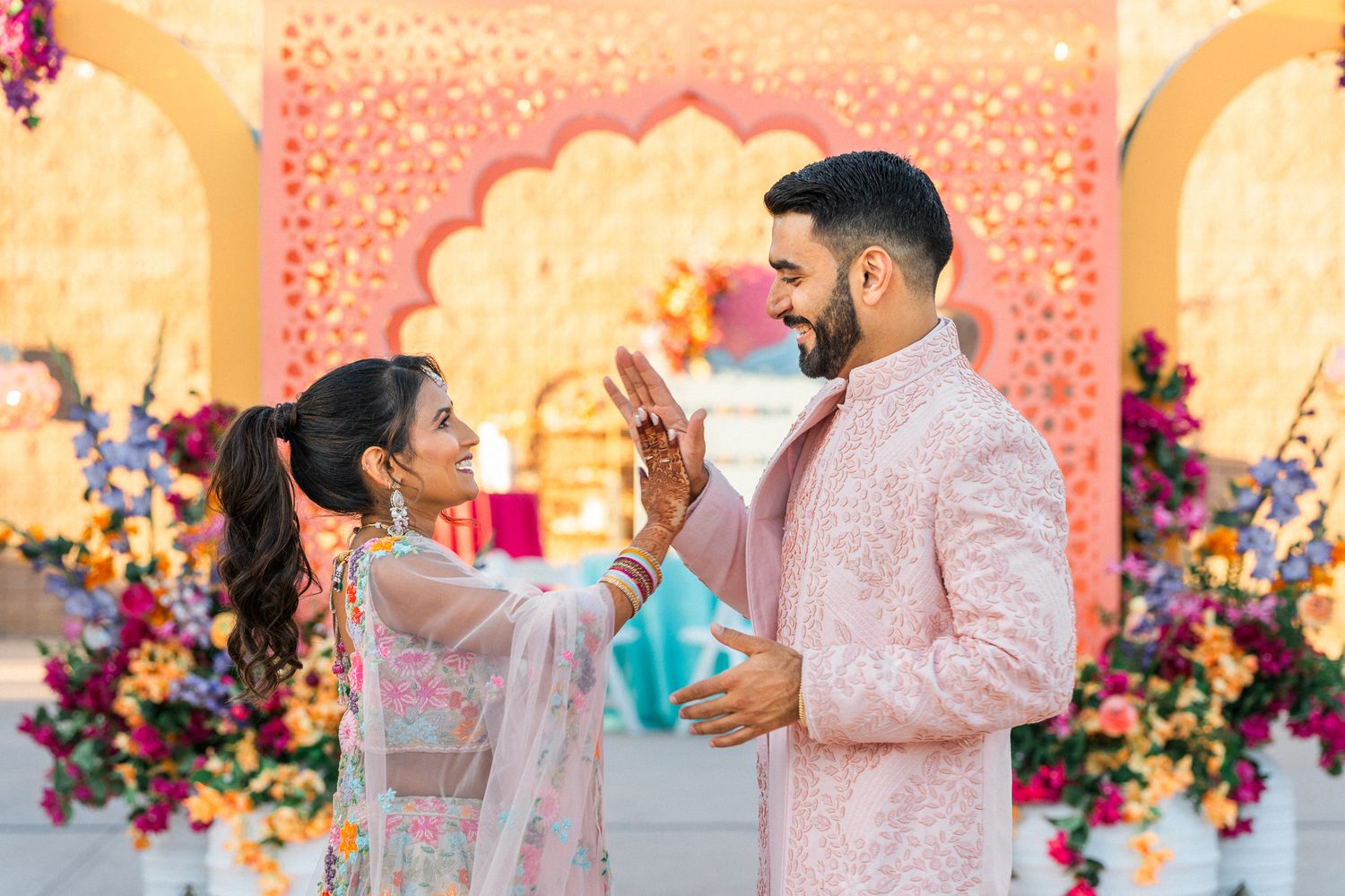 Wedding celebration with vibrant pink and orange floral backdrop and decorative lighting.