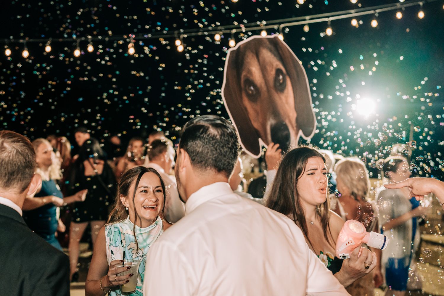 Wedding reception under string lights with festive crowd and party atmosphere.