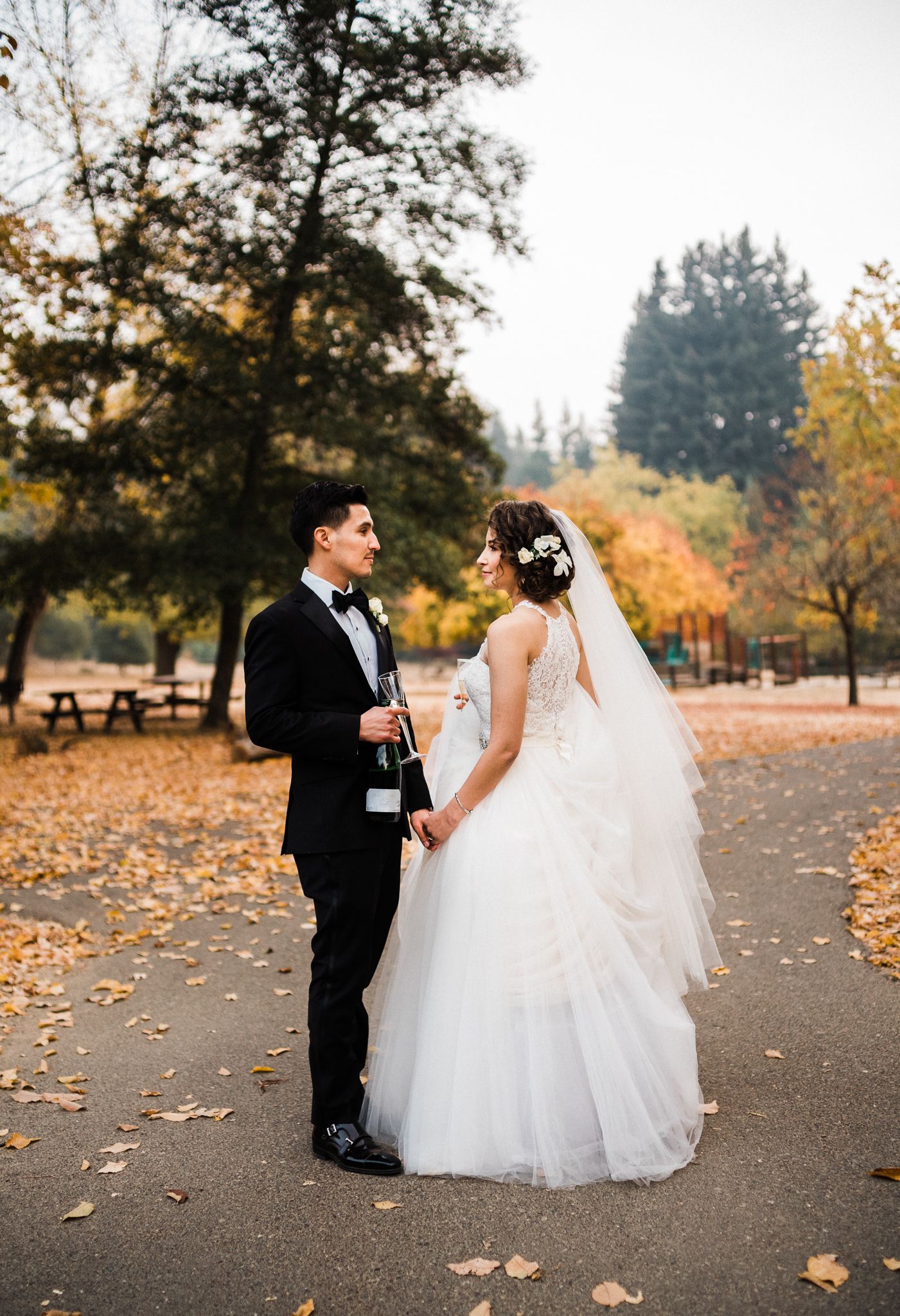 Wedding couple poses on path with autumn leaves scattered around them.