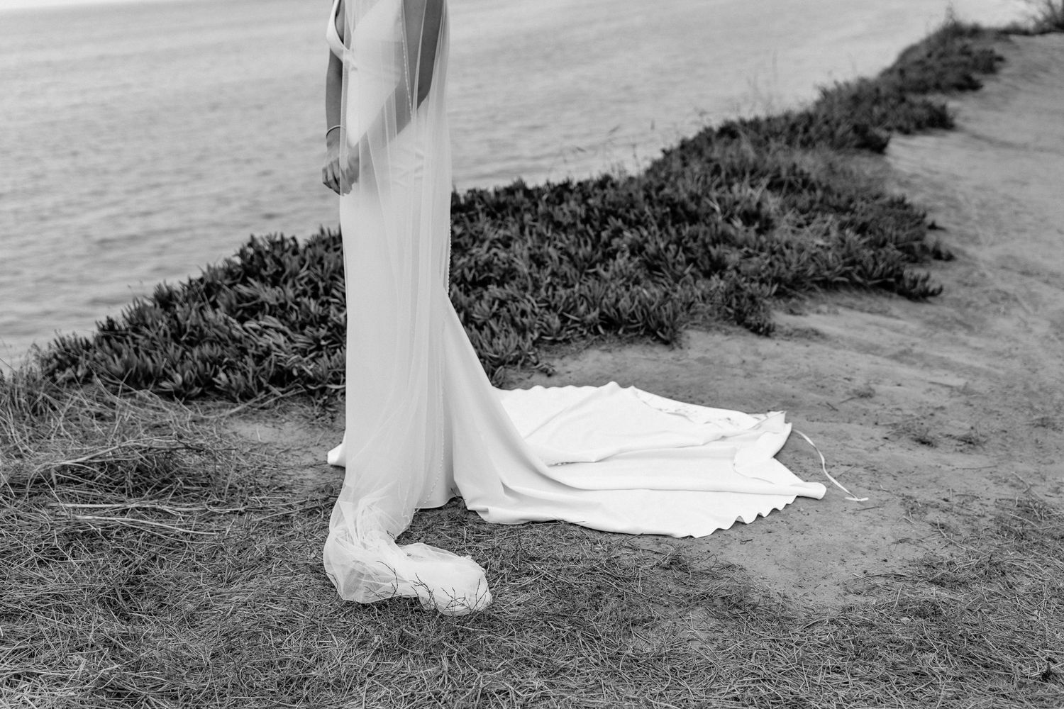 Close-up of white wedding dress hem and shoes on coastal path.