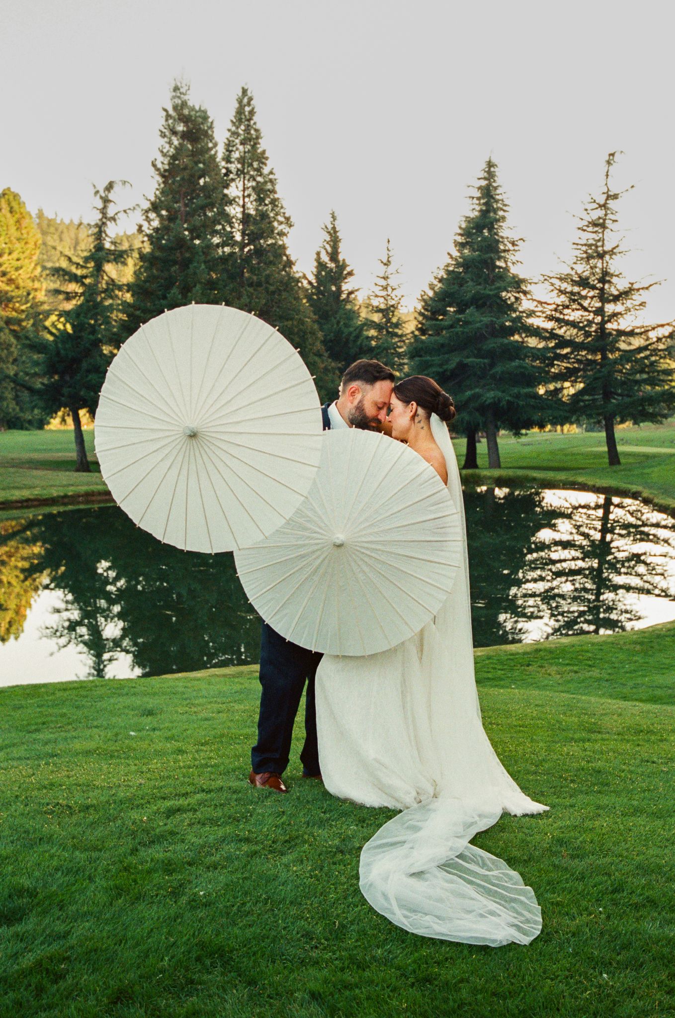 Romantic wedding photo with white parasols against sunset on manicured golf course.