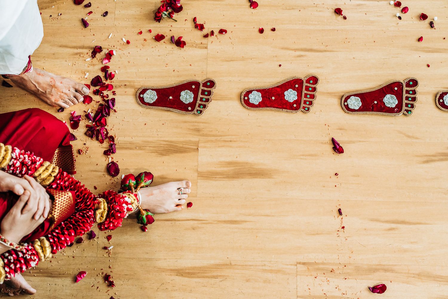 Red rose petals scattered across light wooden floor create romantic atmosphere.