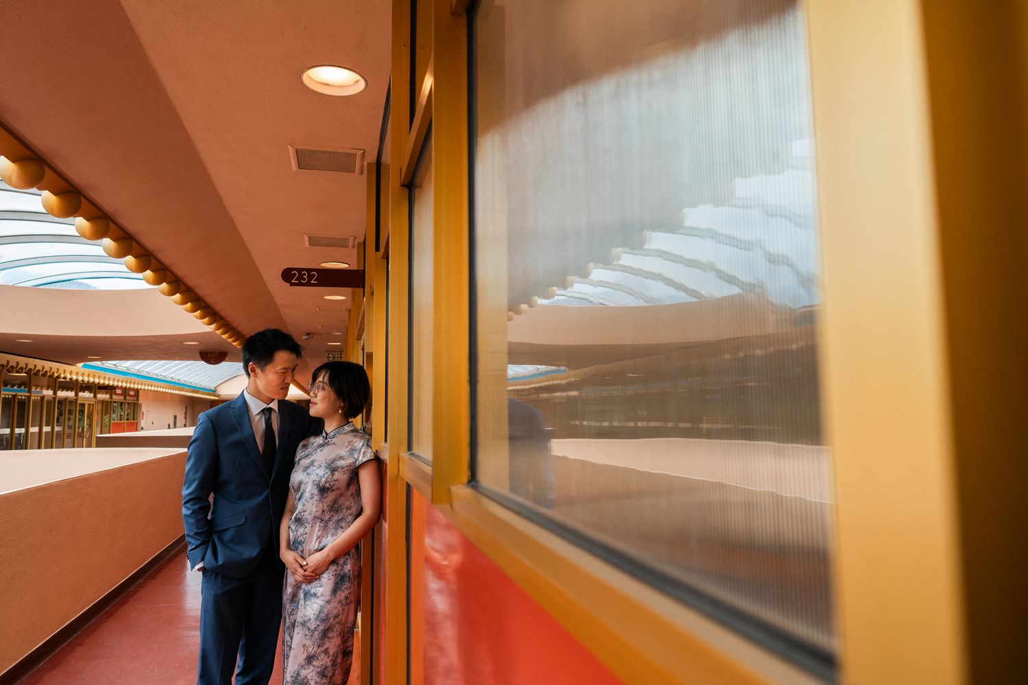 Couple in formal attire sharing an intimate moment in a colorful mid-century modern architectural corridor.