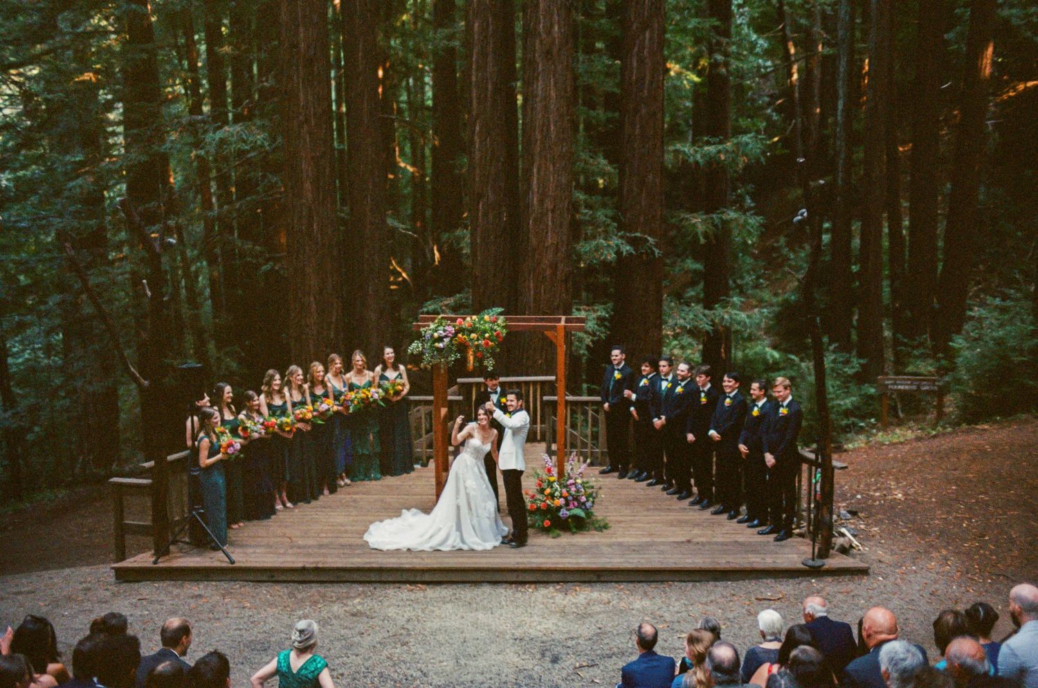 Wide angle view of a wedding ceremony in a majestic redwood forest grove.