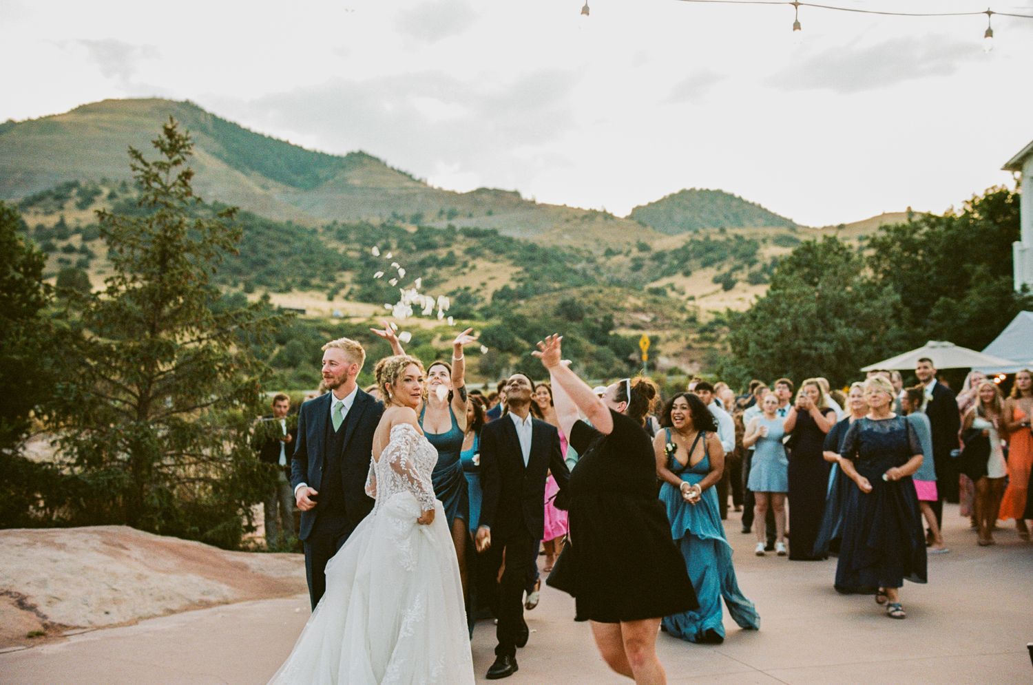 Wedding celebration at sunset with guests dancing outdoors against mountain scenery.