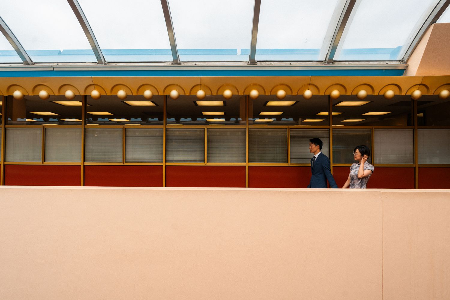 Couple walks along a colorful retro-style balcony with gold lights and red trim during a romantic photoshoot.