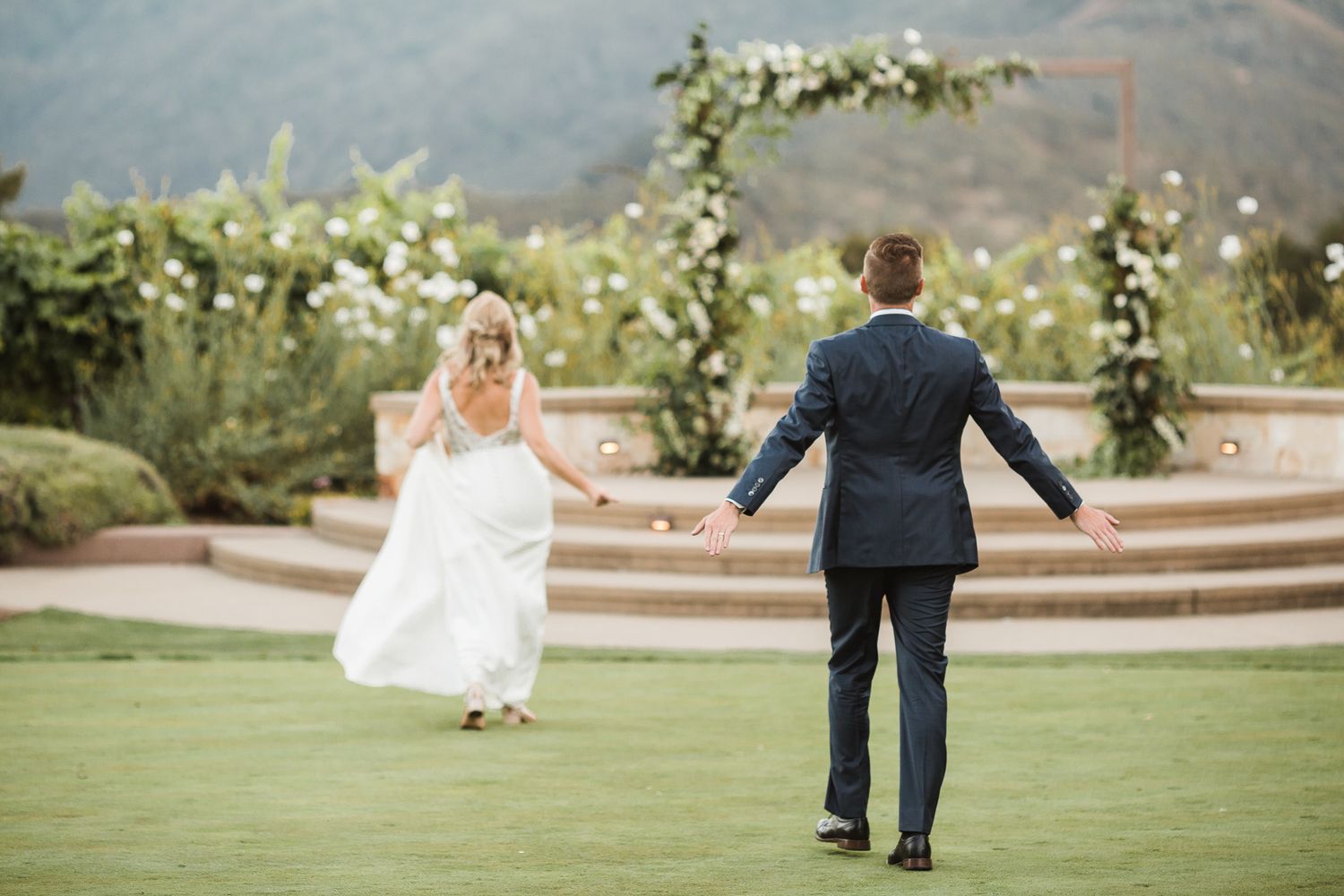 Wedding couple walking together on manicured grounds with stone steps and greenery.