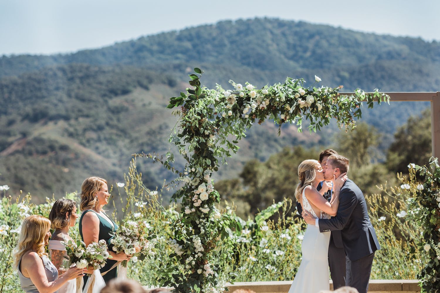 Panoramic view of outdoor wedding ceremony against rolling hills and mountains.