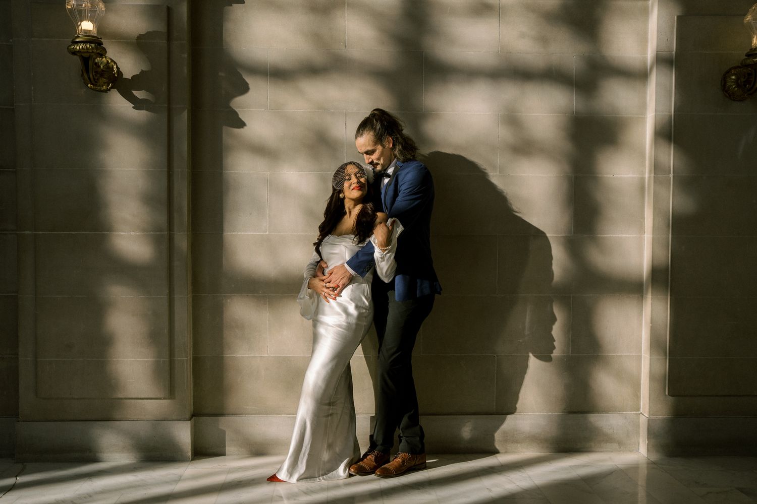 Moody black and white series of newlyweds posing against sunlit wall with dramatic shadows.