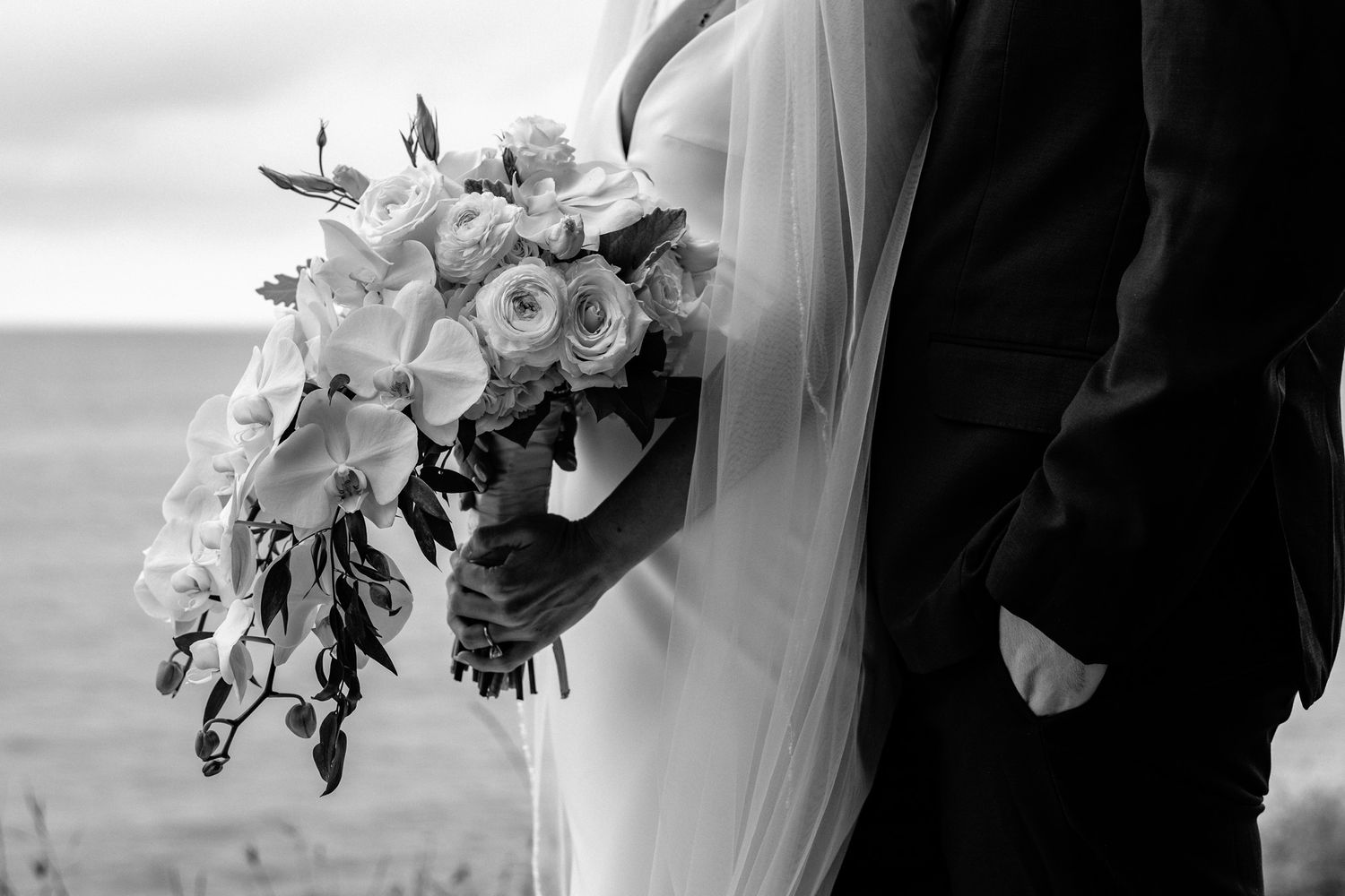 An elegant bridal bouquet of white flowers complements a seaside wedding scene.