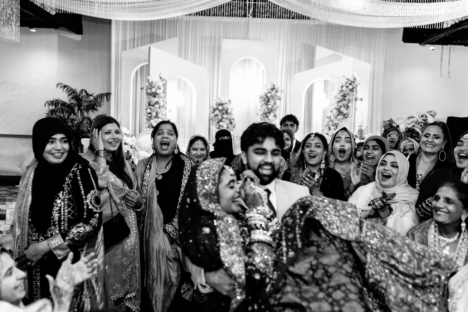 Black and white photo of wedding guests celebrating at an indoor reception.
