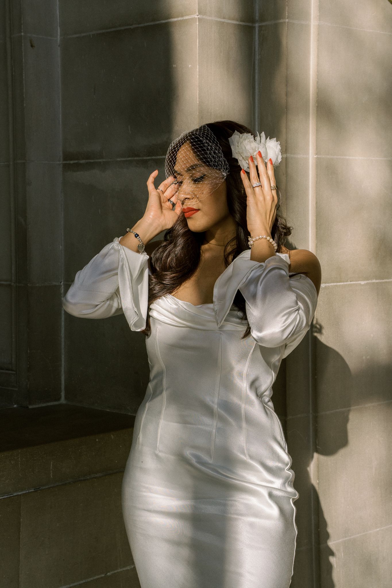 Playful bride in white dress poses against stone wall with dramatic lighting.