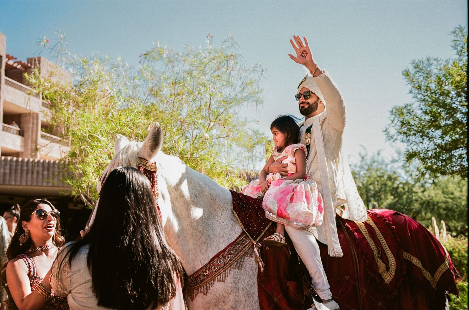 Wedding guests celebrate outdoors with raised hands against a bright blue sky.
