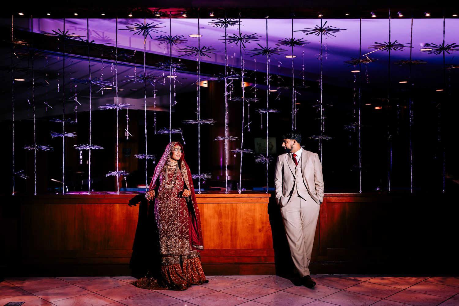 Wedding reception scene with purple ambient lighting and hanging decorative elements.