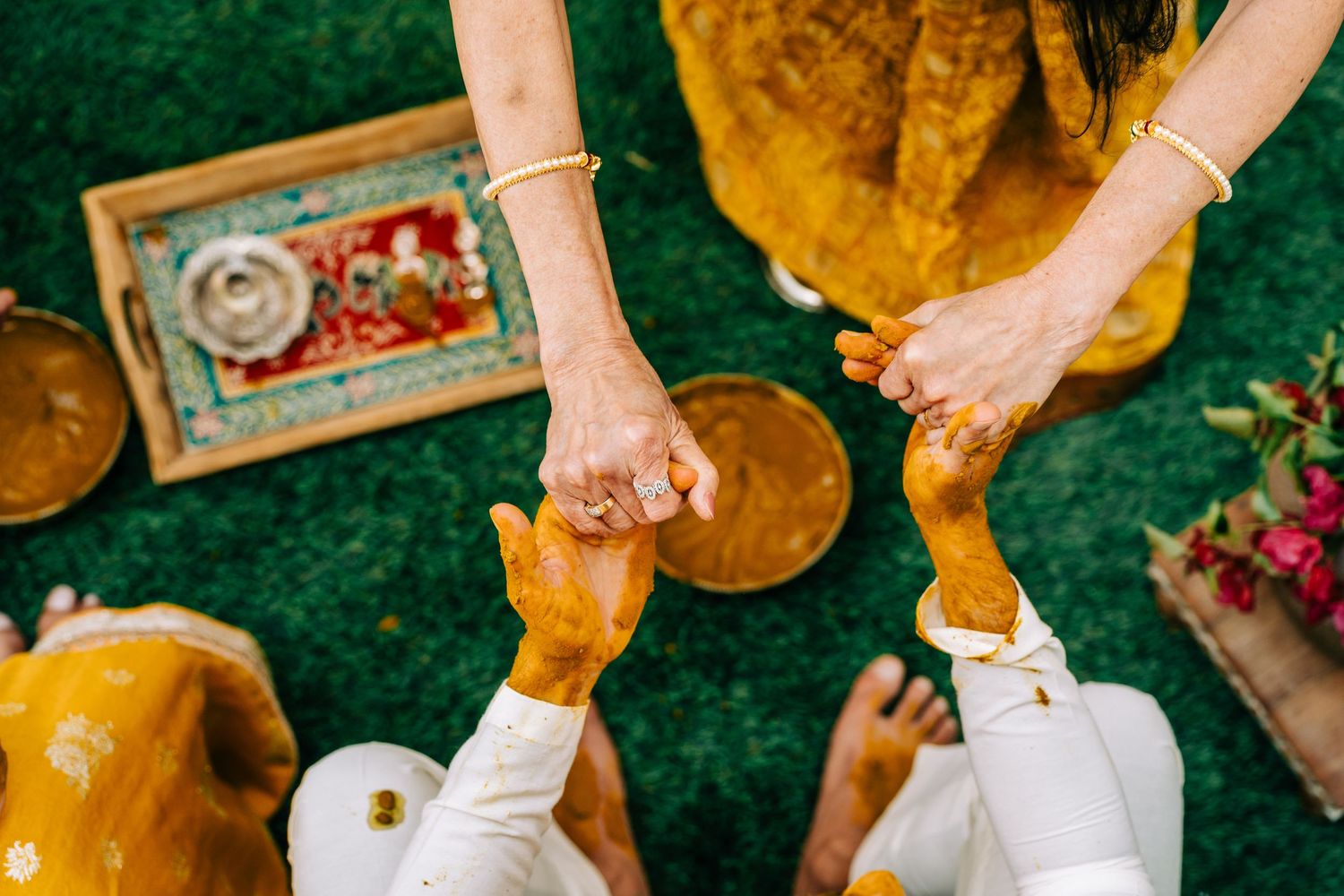 Overhead view of hands participating in a traditional Indian Haldi ceremony with turmeric paste.