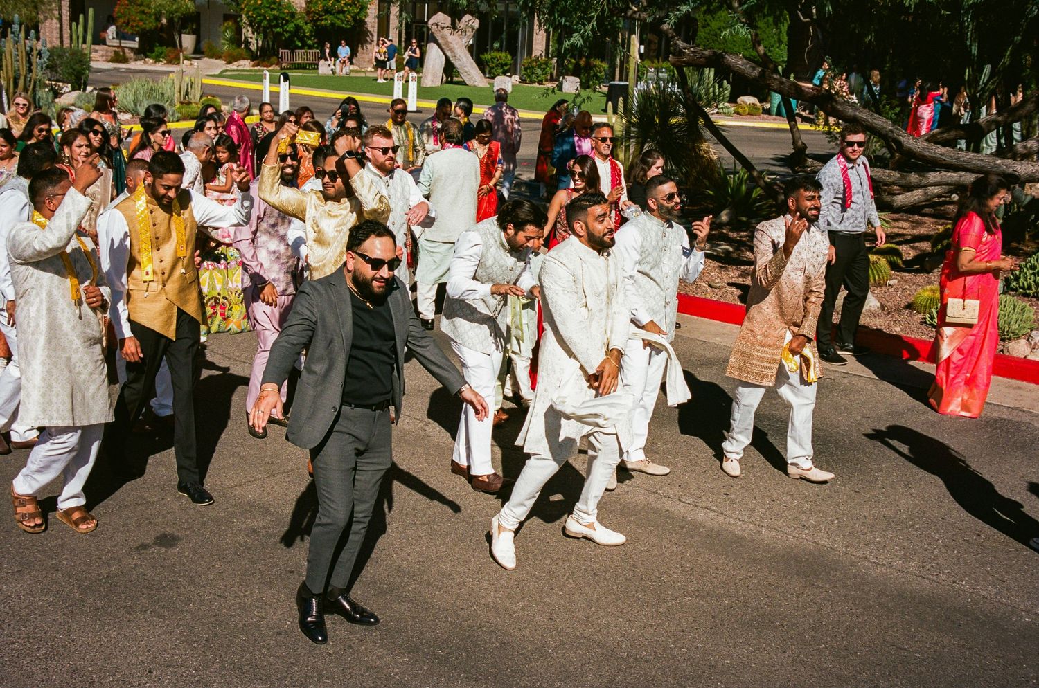 Joyful wedding party dancing and celebrating on street during daytime procession.