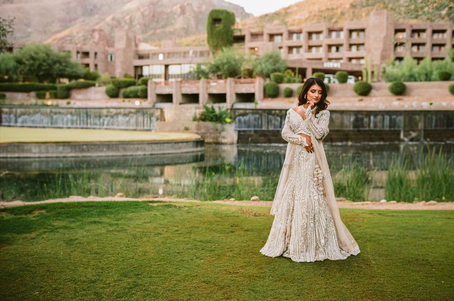 A stunning cream lace gown photographed on a lawn with desert mountains in the background.