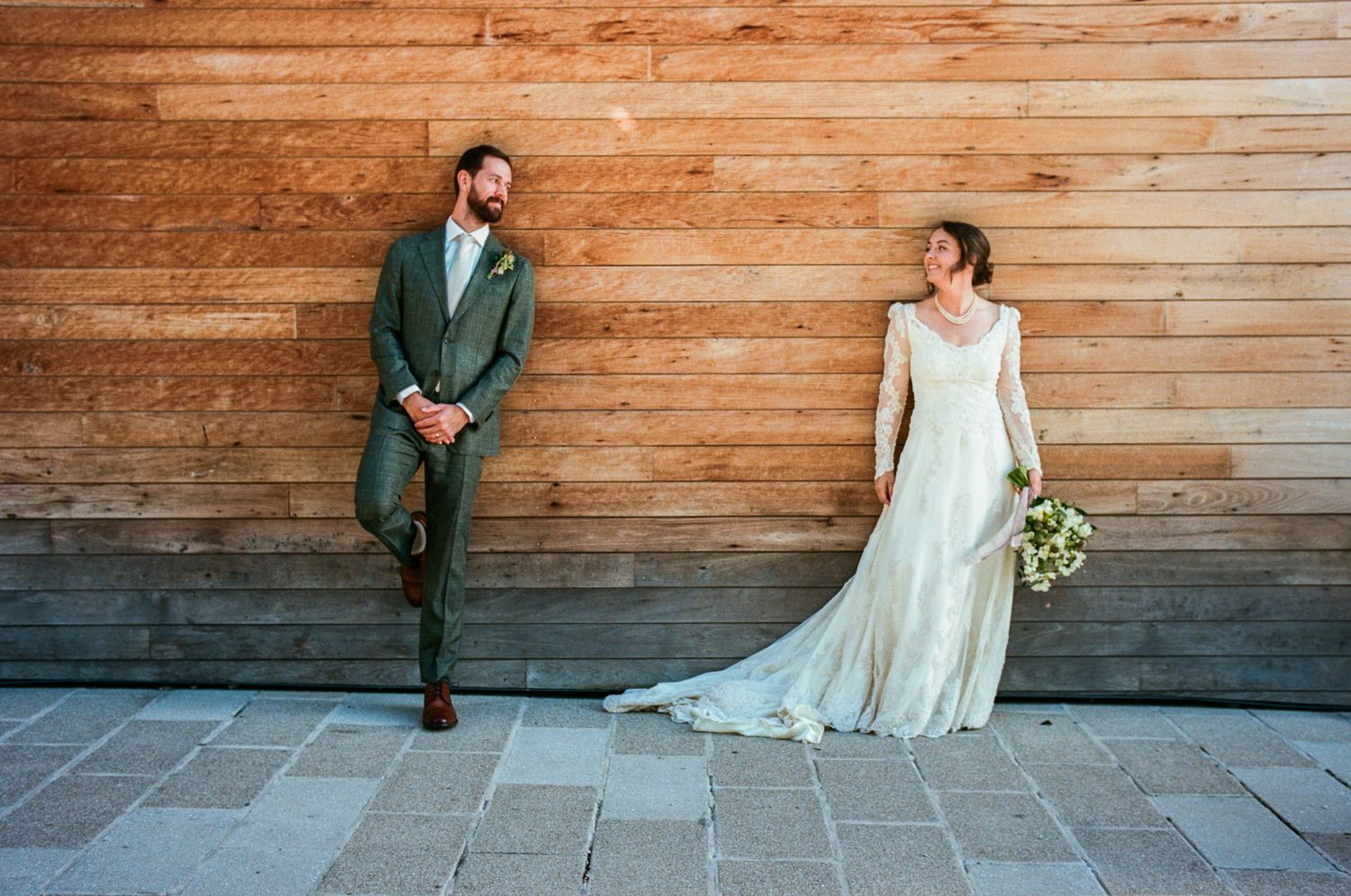 A wedding couple poses against a rustic wooden wall backdrop for romantic portraits.