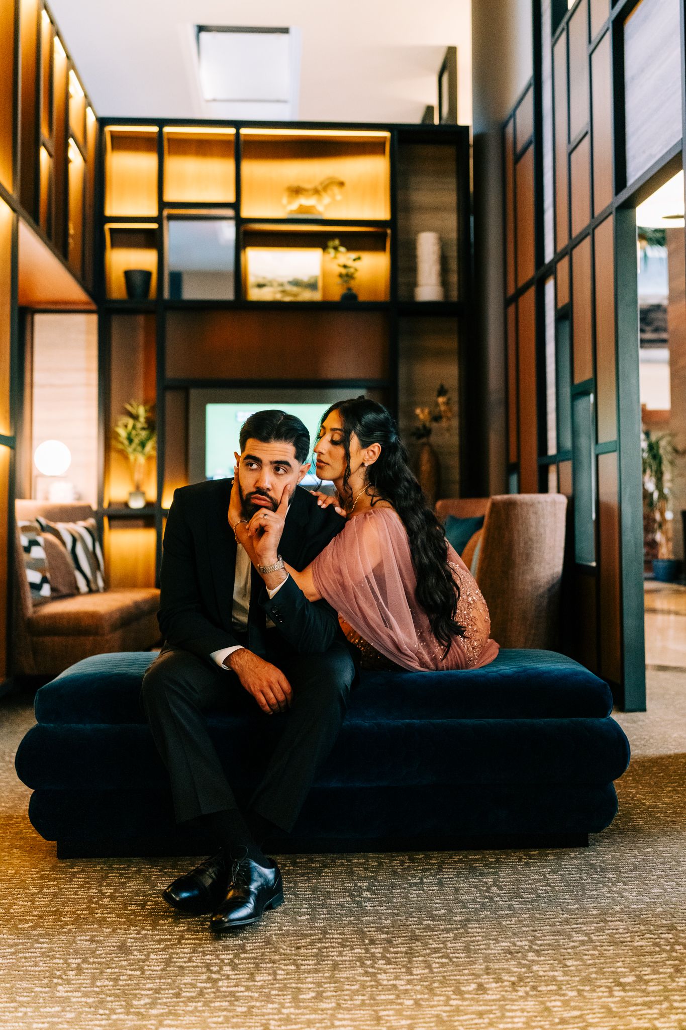 A couple lounges on a modern blue sofa in an elegant indoor setting with warm lighting.