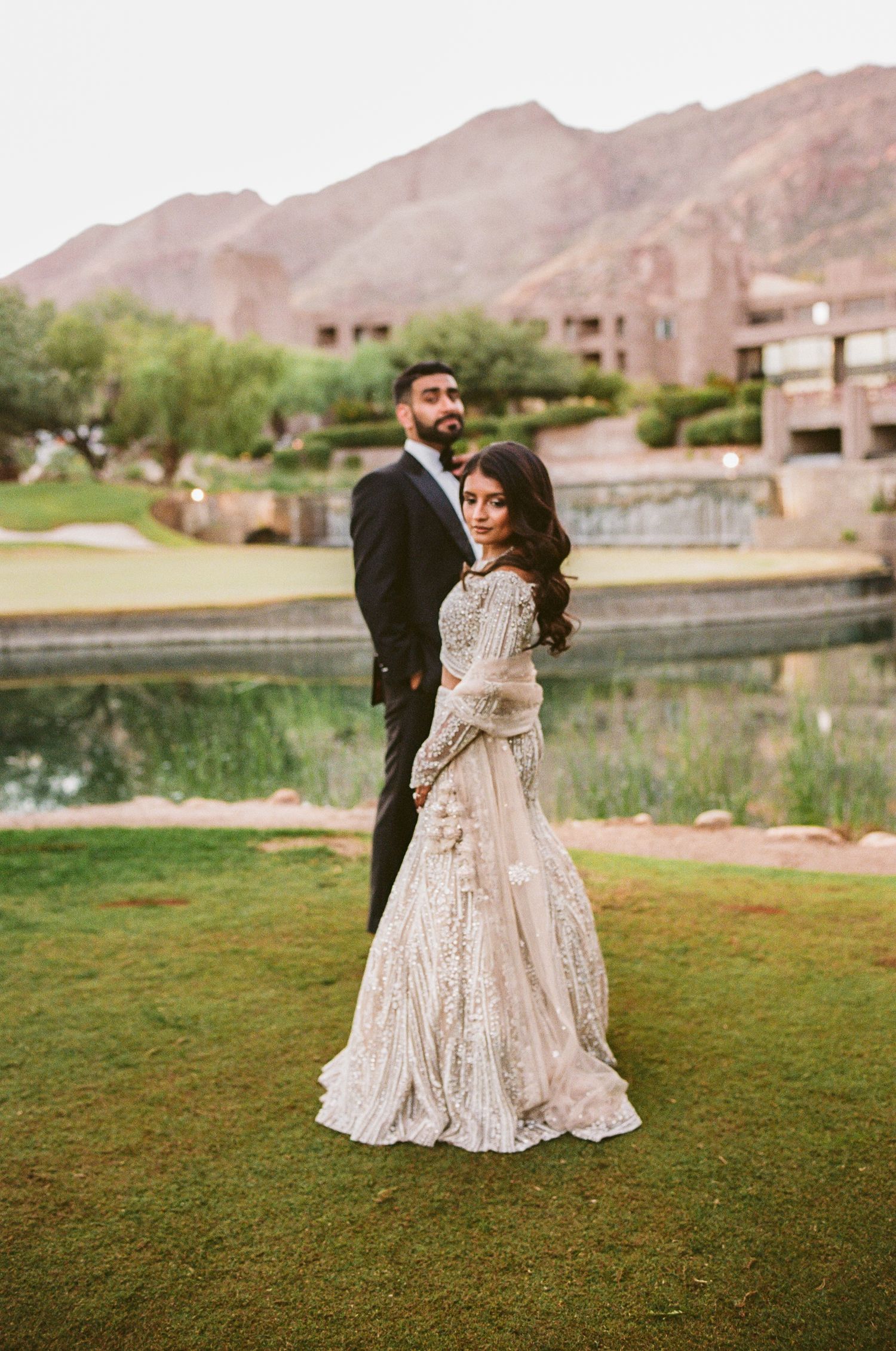 A couple dances together on a grassy lawn with mountains in the background at sunset.