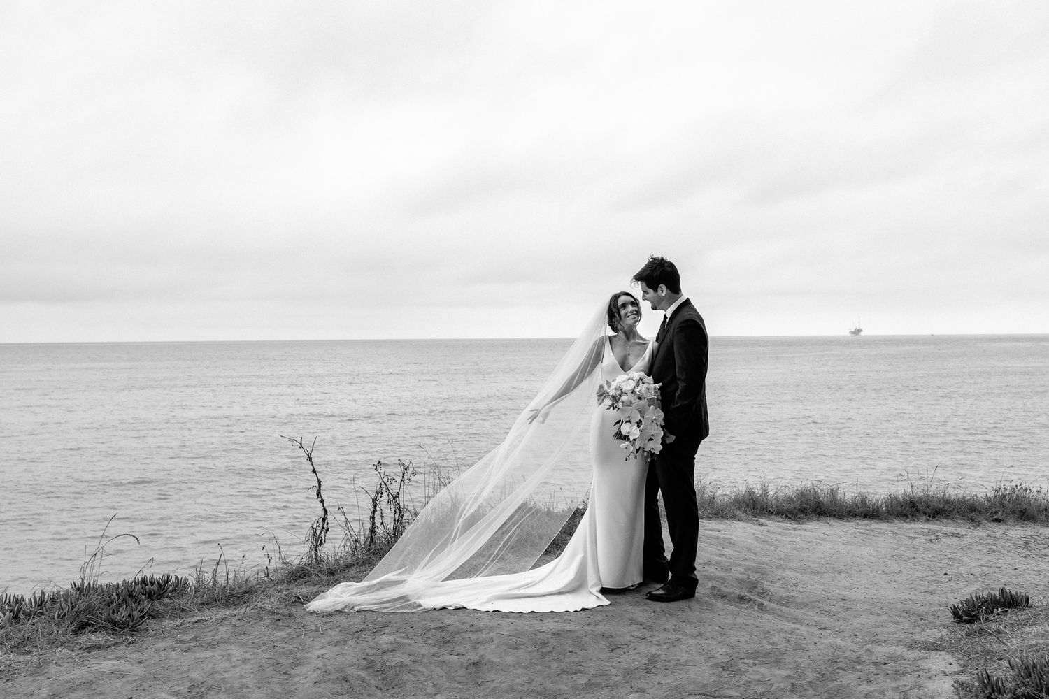 Couple sits together on coastal cliffs during their wedding photoshoot.