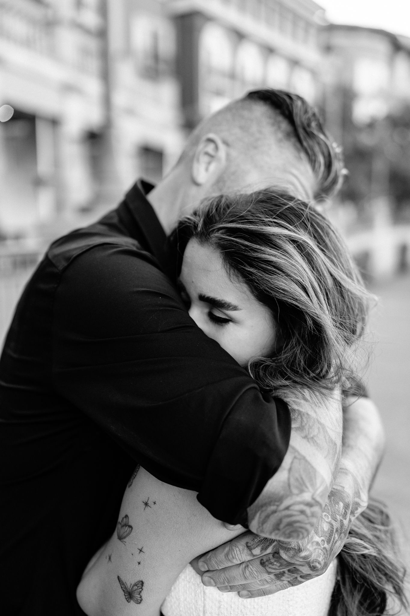 Black and white romantic portrait of a couple embracing, showing tattoos on their arms.