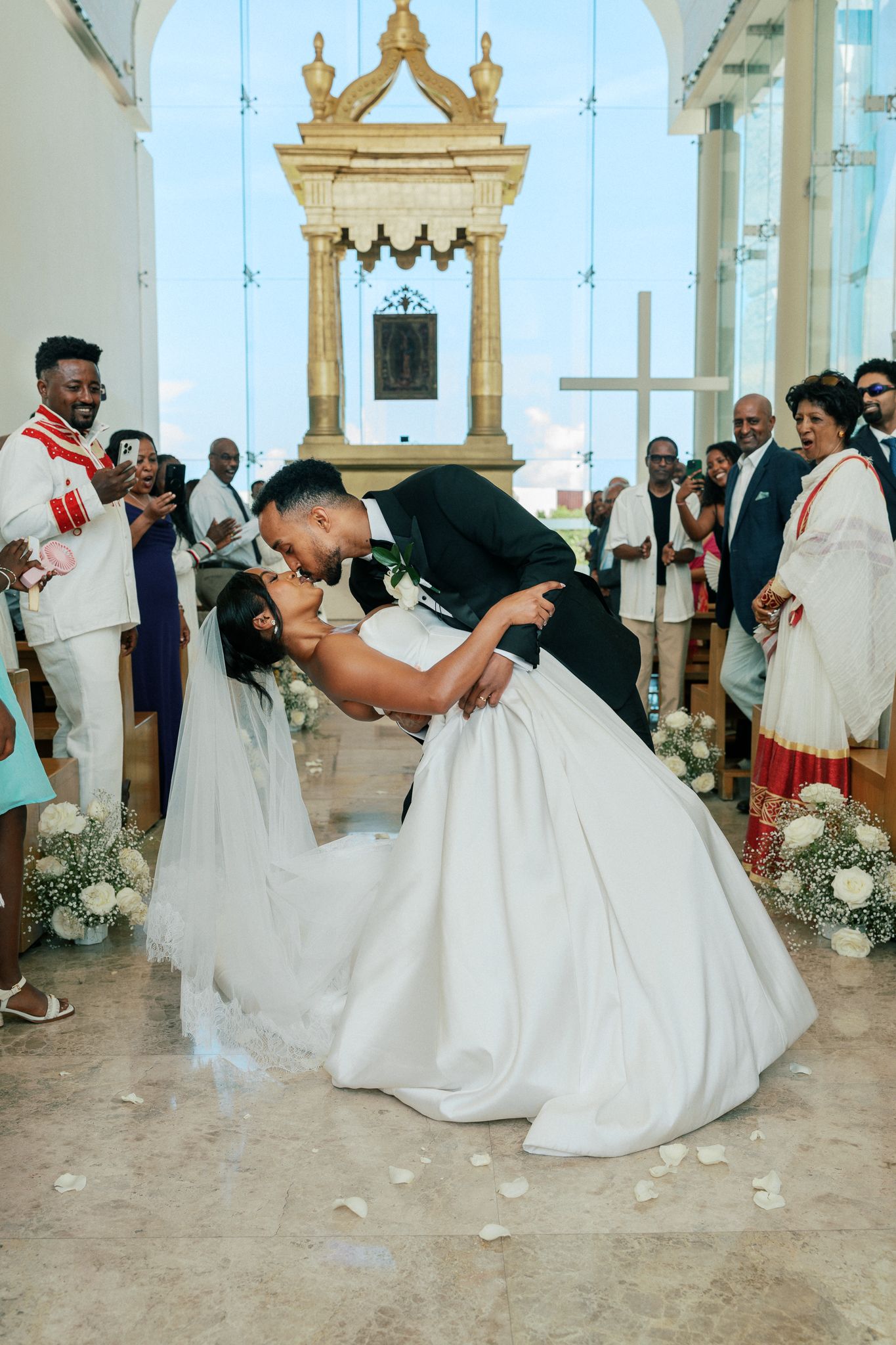 Bride and groom share a romantic dip kiss at the altar during their church wedding ceremony with guests watching.