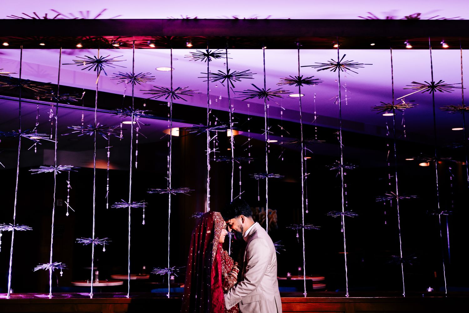 Wedding reception venue with purple lighting and hanging crystal decorations.