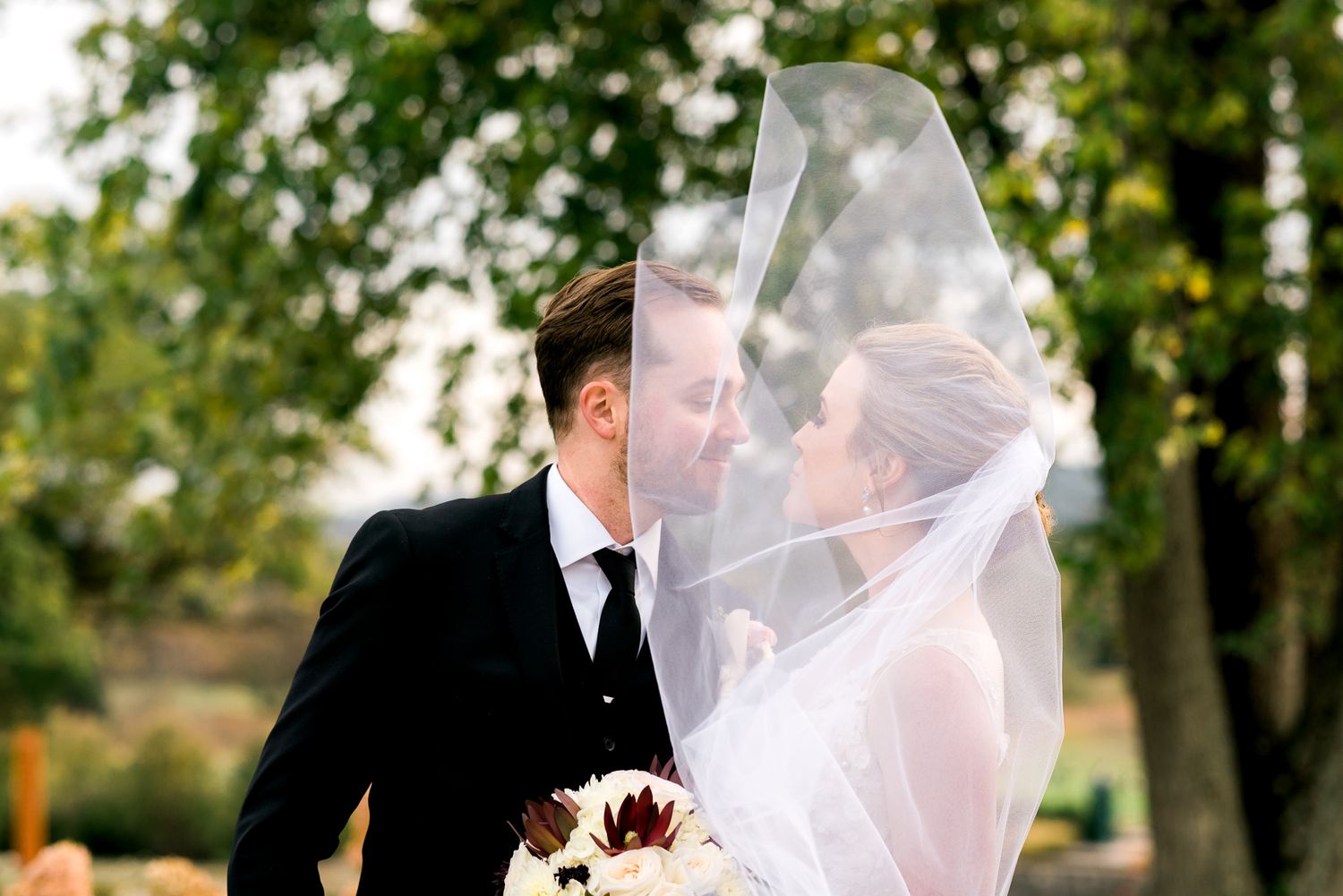 Wedding couple shares intimate moments outdoors with flowing veil in natural light.