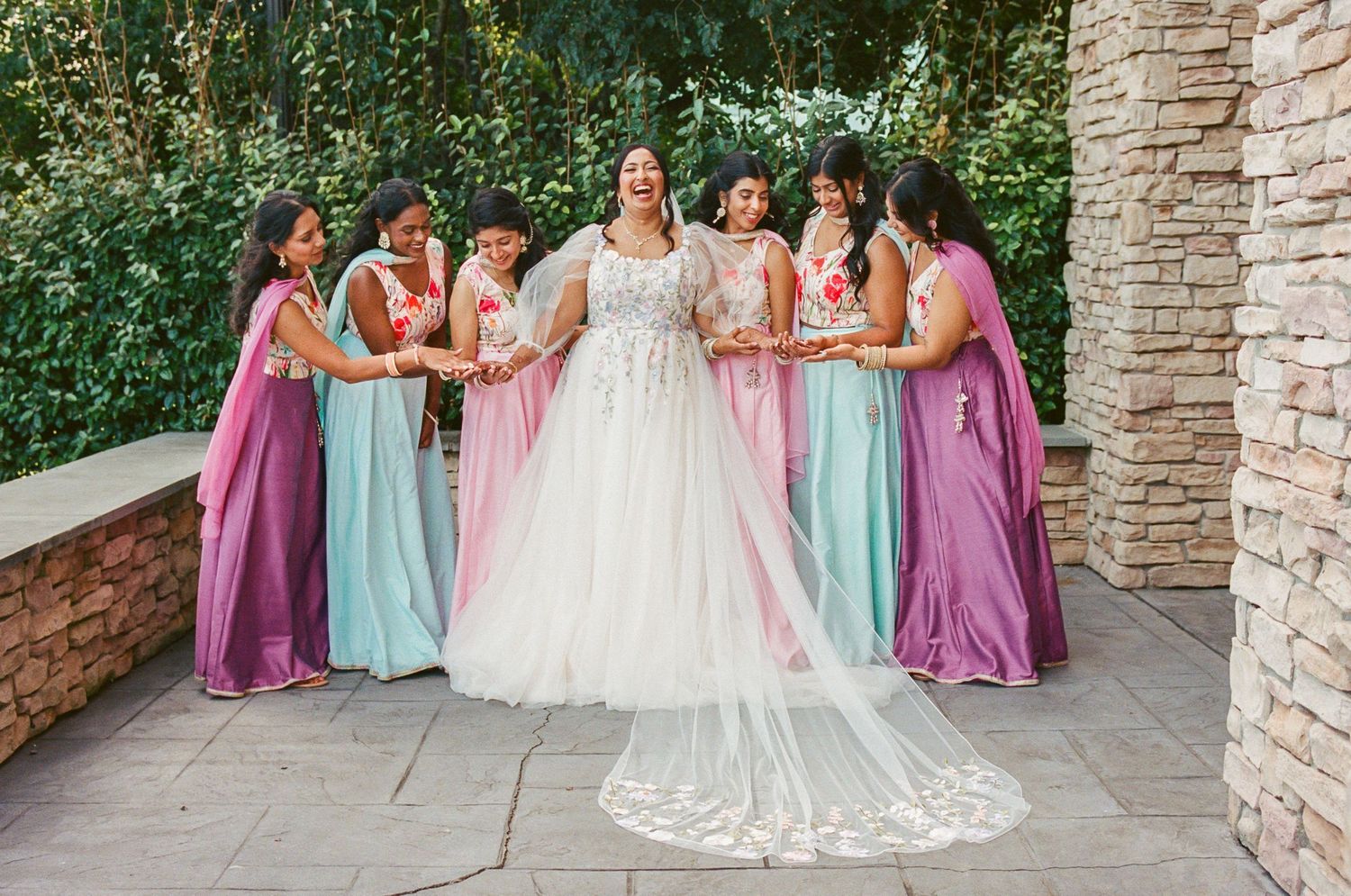 Wedding party poses against stone wall wearing purple and mint colored dresses.
