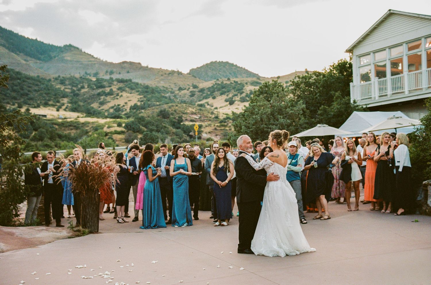 Wedding reception guests gather outdoors as newlyweds share first dance with mountain scenery.
