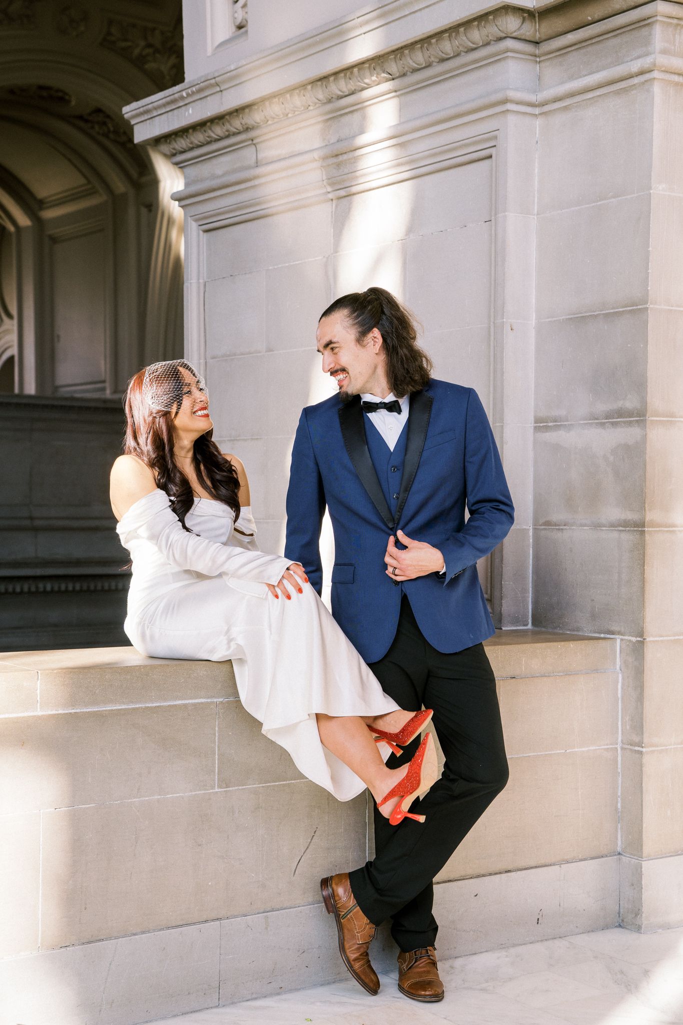 Playful wedding portraits against classic white stone architecture in sunlight.