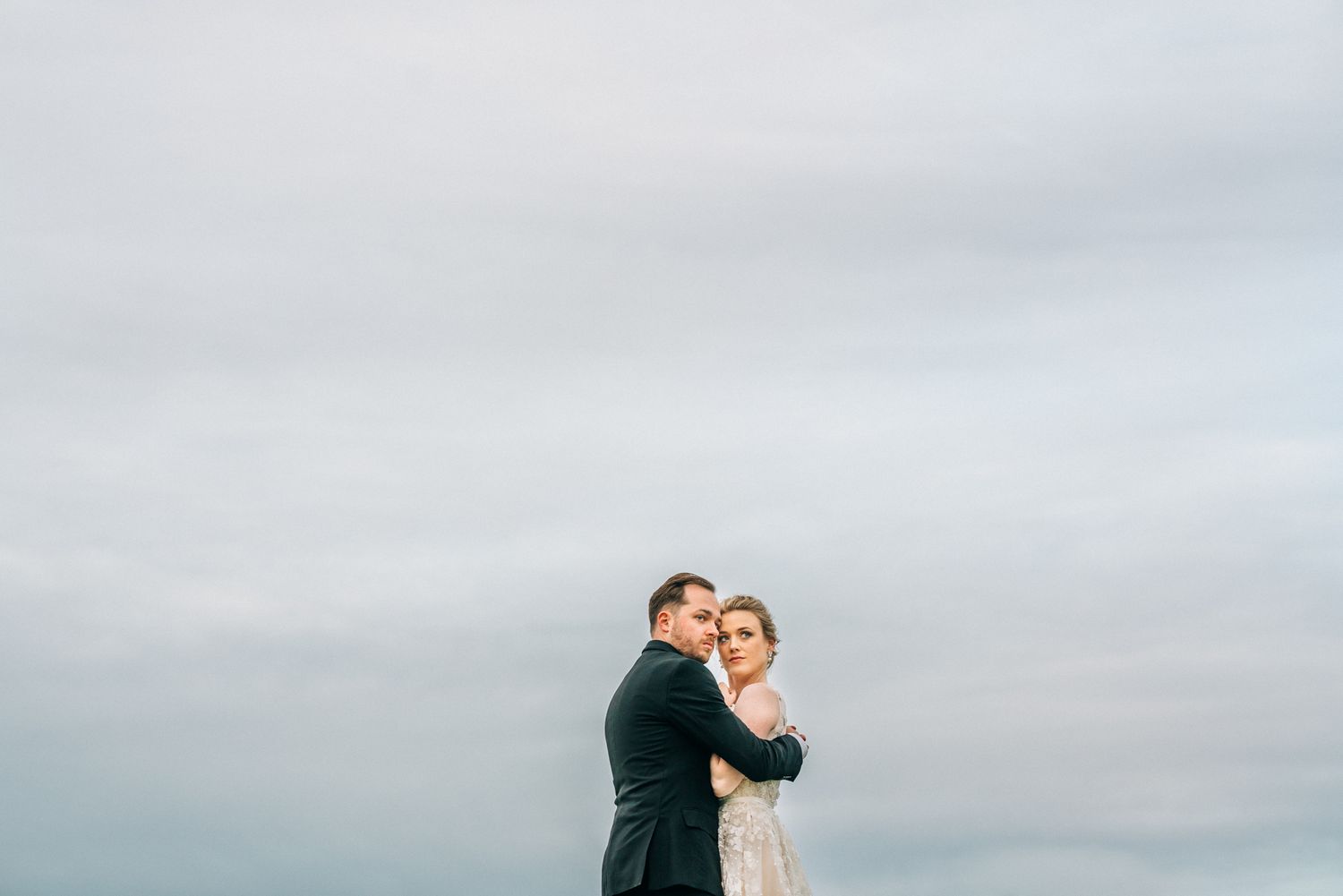 Romantic outdoor wedding portrait against cloudy sky.