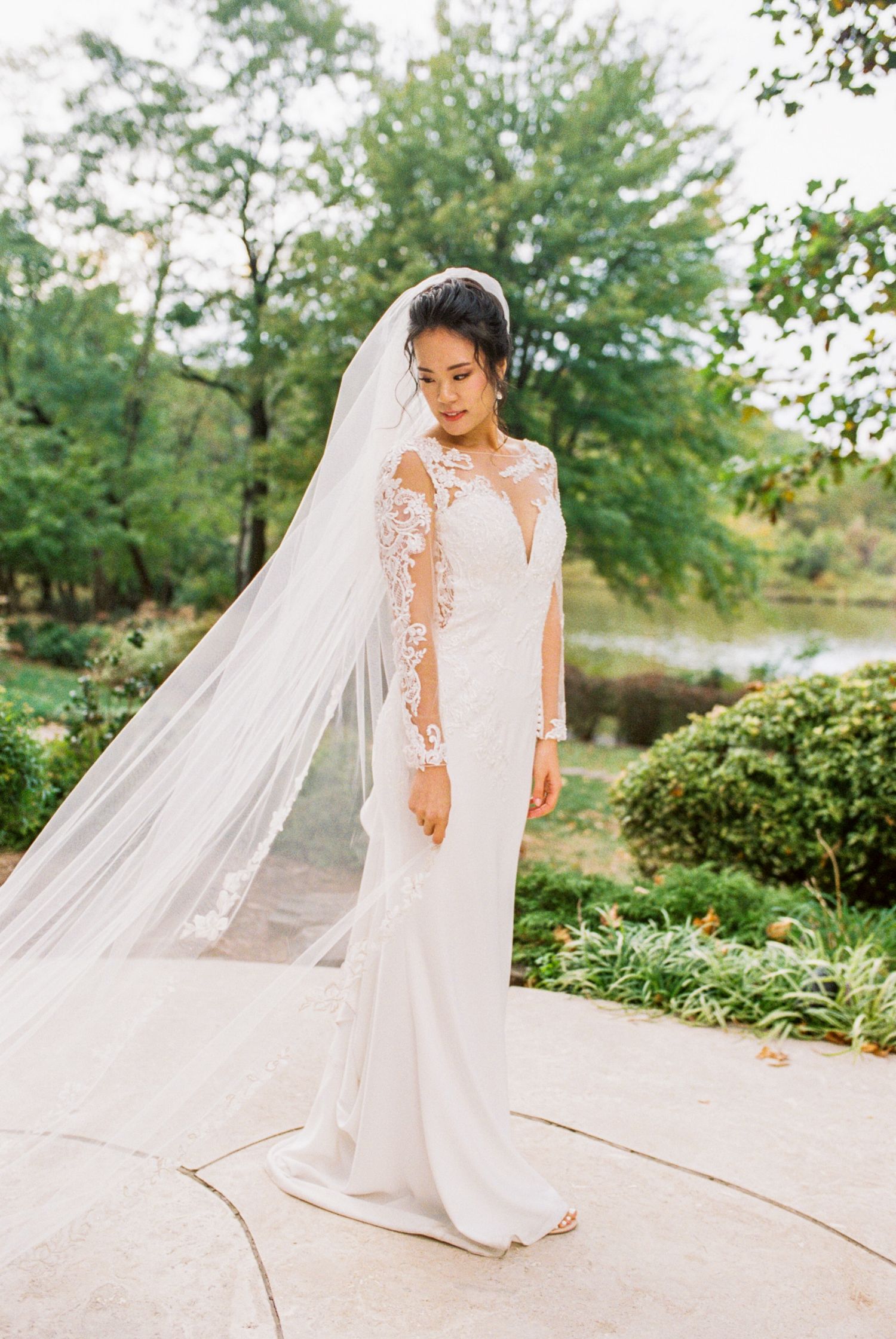 Full-length bridal portraits showing flowing white wedding dress with cathedral veil in garden setting.