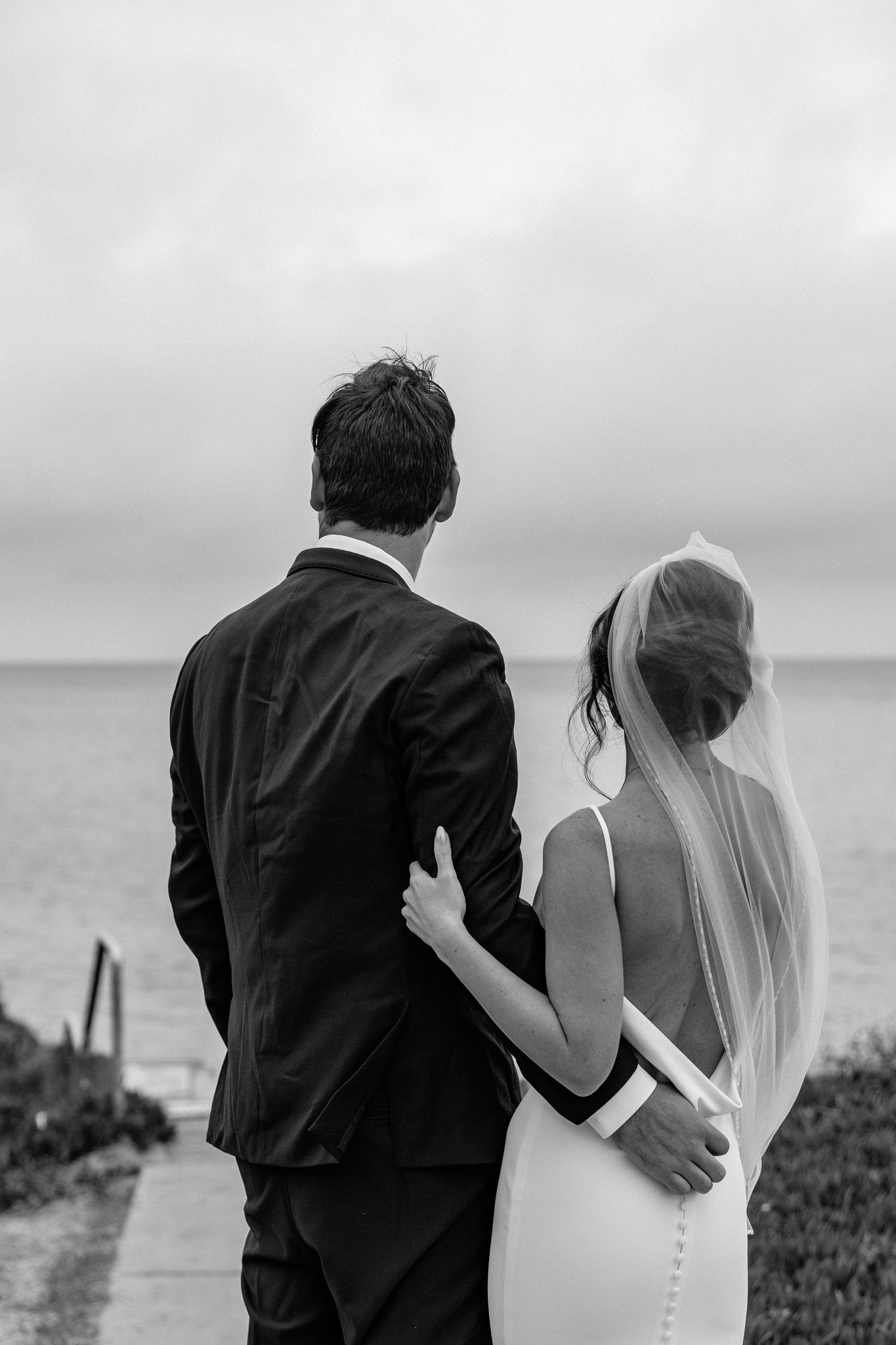 Black and white photos capture tender moments between newlyweds on a coastal cliff.