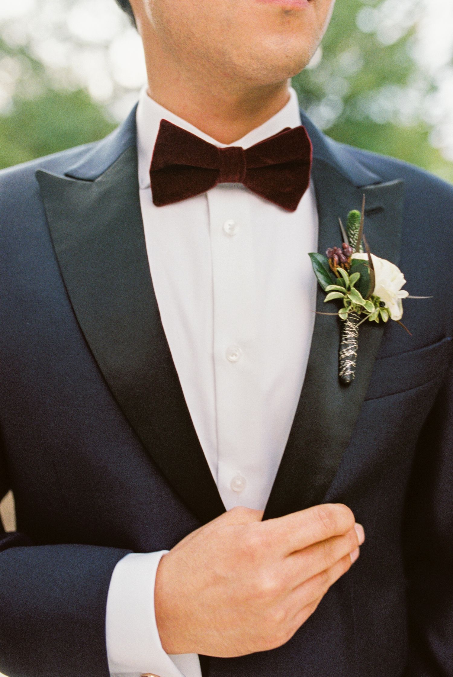 Close-up details of groomsmen in black tuxedos with bow ties and boutonnières at an elegant wedding.