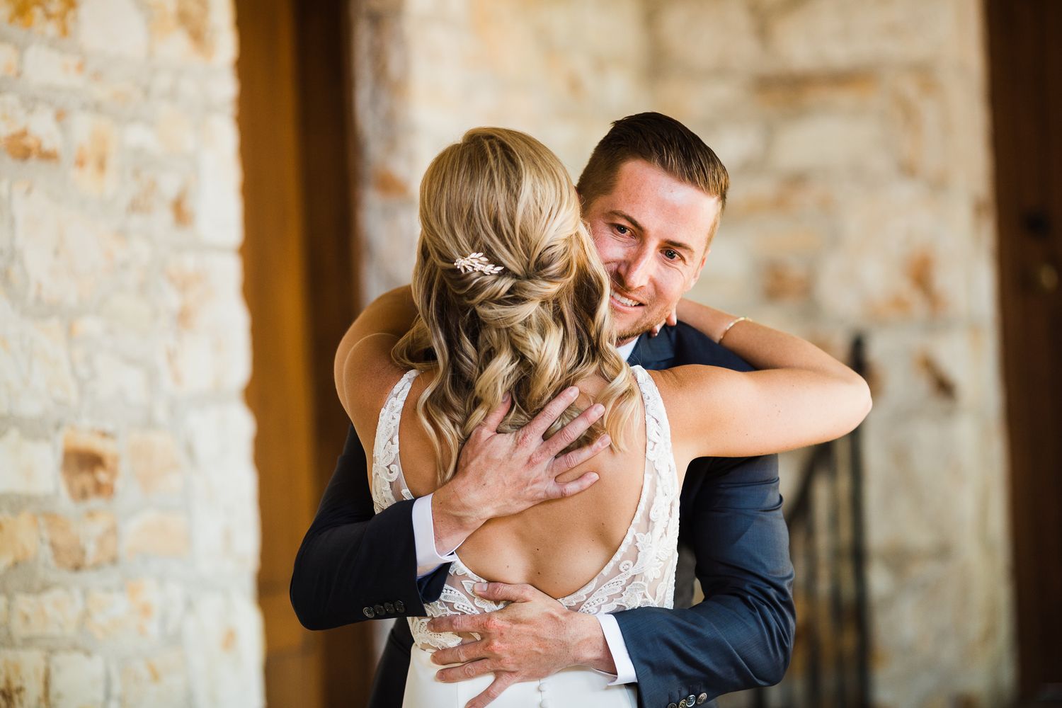 Emotional first look moment captured in front of a rustic stone wall.
