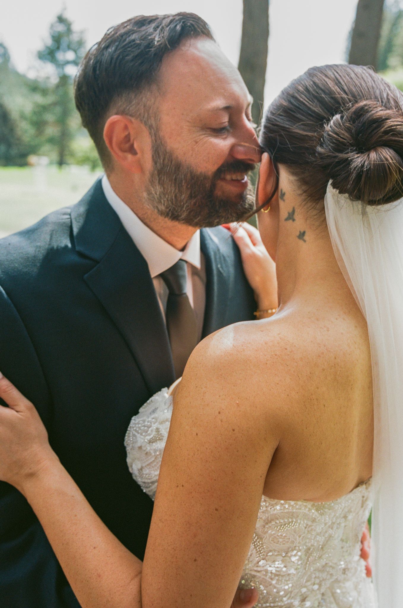 A bride and groom share an intimate moment, almost kissing, as she displays a delicate bird neck tattoo in her wedding dress.