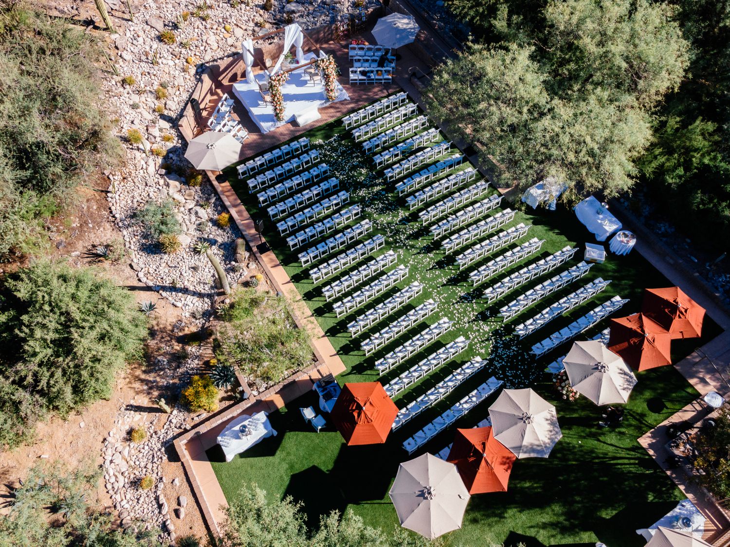 Aerial view of an outdoor wedding ceremony setup with rows of white chairs and umbrellas.