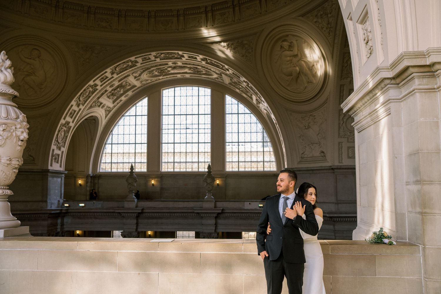 A couple dances together in an elegant historic building with ornate architecture and arched windows.